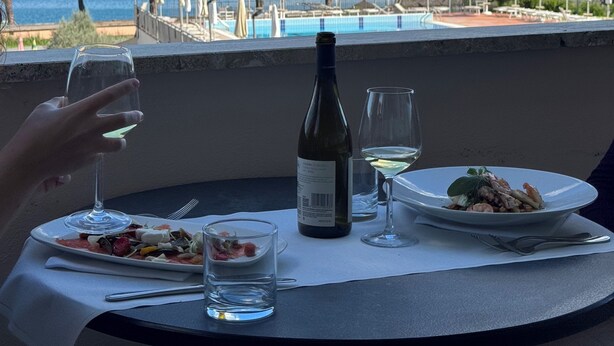 A table with a bottle of wine, glasses, and plates of food, overlooking a pool and trees. - HA HOTEL (Bracciano)