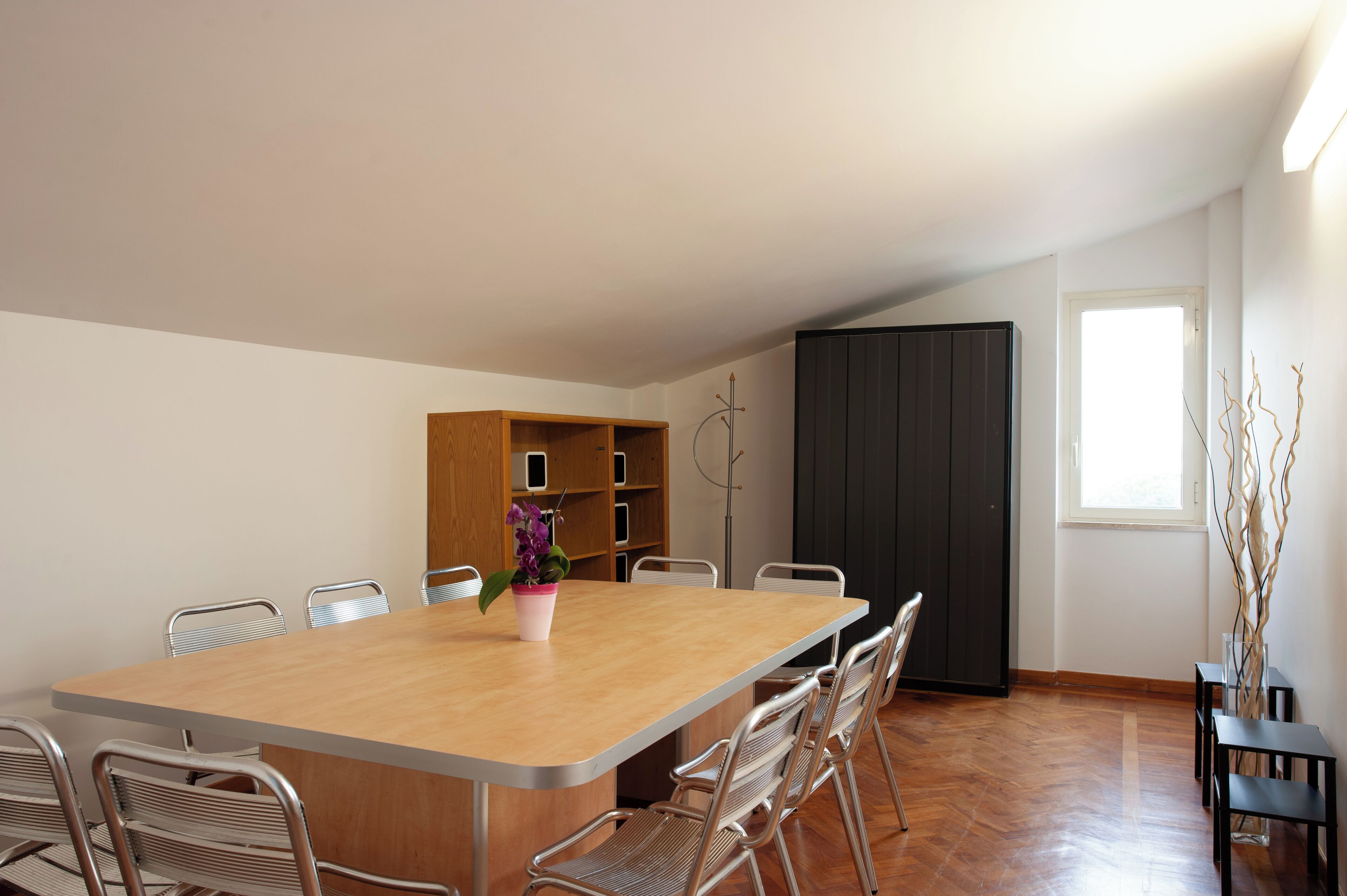 Une pièce spacieuse avec une grande table en bois et des chaises en métal, une bibliothèque et une grande fenêtre.