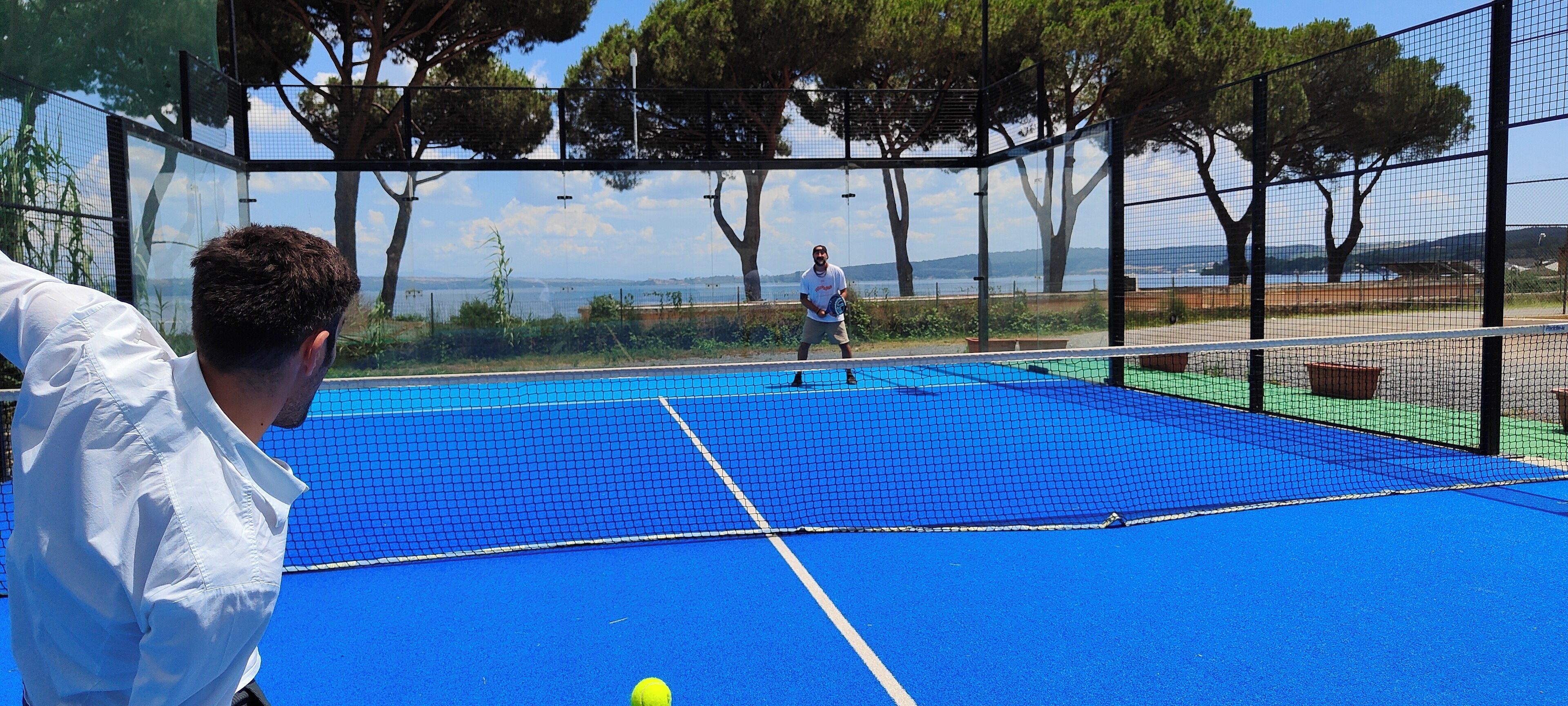Ein Tennisplatz mit Netz, umgeben von Bäumen und blauem Himmel.