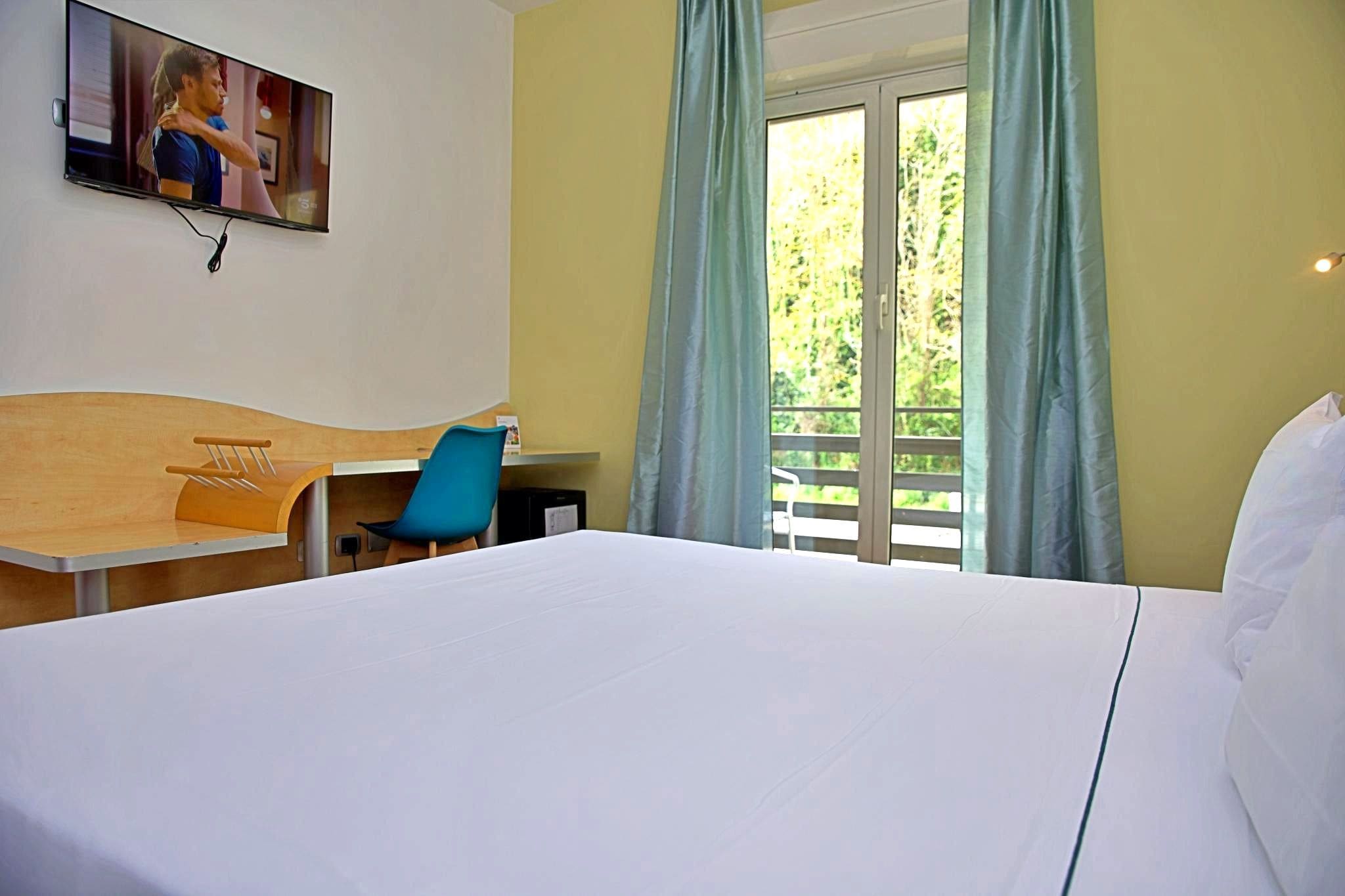 A hotel room with a bed, a desk, a chair, a TV, and a window with curtains.