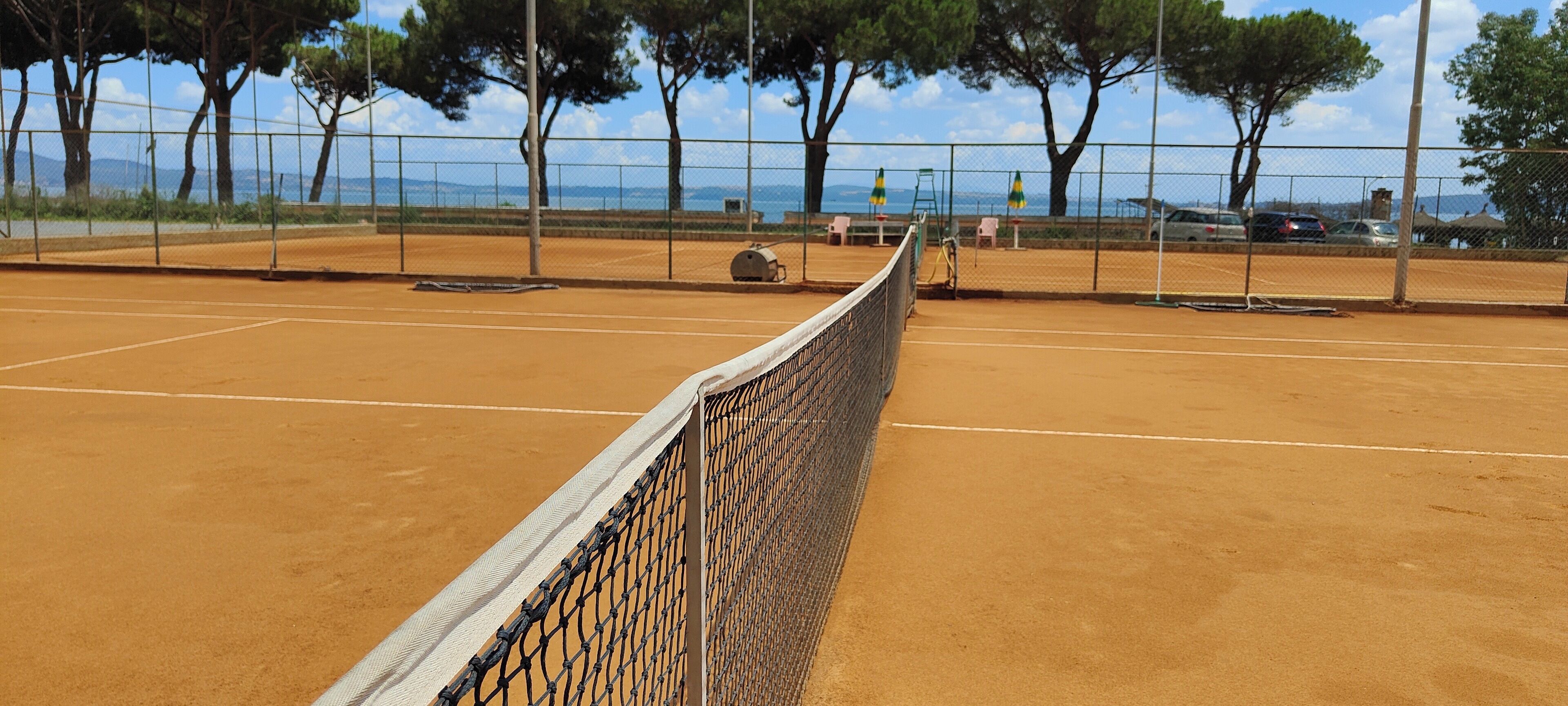 A tennis court with a net, surrounded by trees and a fence.