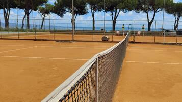 A tennis court with a net, surrounded by trees and a fence.