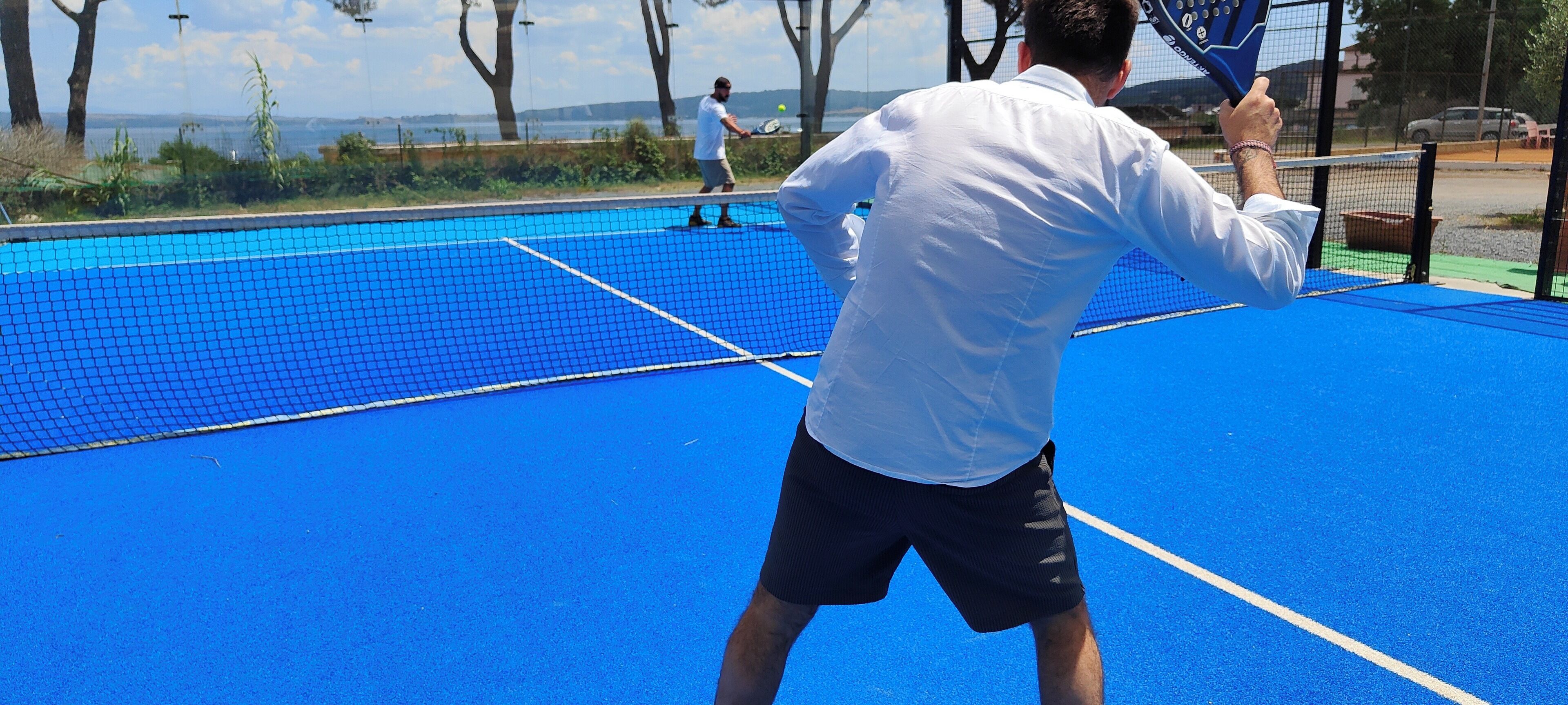Una cancha de tenis con una red, una persona con camisa y pantón blancos, y otra persona con camisa y pantón negros.