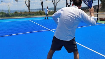 Una cancha de tenis con una red, una persona con camisa y pantón blancos, y otra persona con camisa y pantón negros.