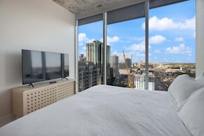 Camera d'albergo moderna con un letto grande, una televisione su un mobile in legno e vista sulla città attraverso ampie finestre a tutta parete.