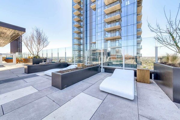 Una terrazza sul tetto con arredi moderni, un edificio in vetro sullo sfondo e cielo sereno.