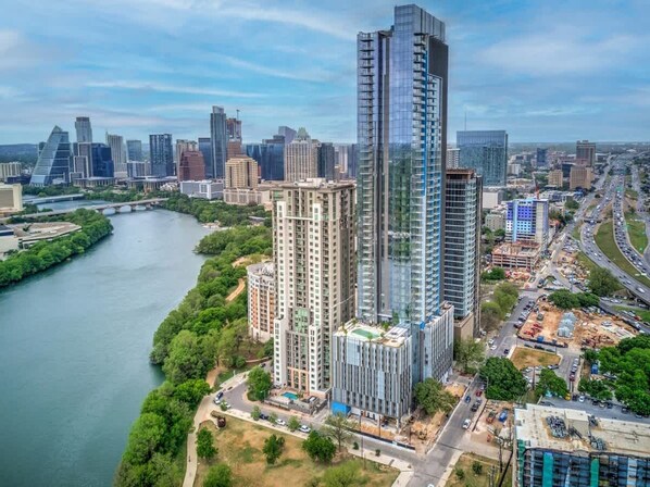 Un edificio moderno de gran altura con fachada de vidrio, rodeado por un río y otras construcciones urbanas.