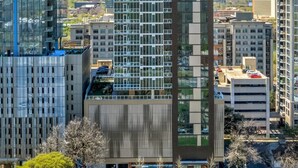 Ein Hochhaus mit moderner Glasfassade, umgeben von anderen Gebäuden und einem Parkplatz mit Autos.