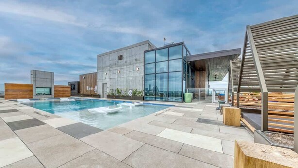Ein Poolbereich auf dem Dach mit einem modernen Gebäude, einer Holzterrasse und einer Glasfassade.