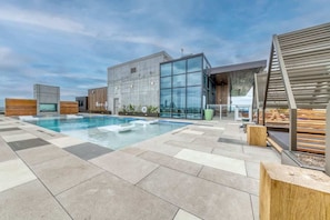 A rooftop pool area with a modern building, a wooden deck, and a glass facade. - Rainey St 1BR Luxury Condo • Rooftop Pool & Gym (Austin)
