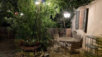 Een terras met een ronde tafel en stoelen, omgeven door potplanten en een kleine fontein.