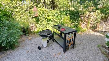 Un jardín con una parrilla, una mesa pequeña con un farolillo y una jaula de pájaros.