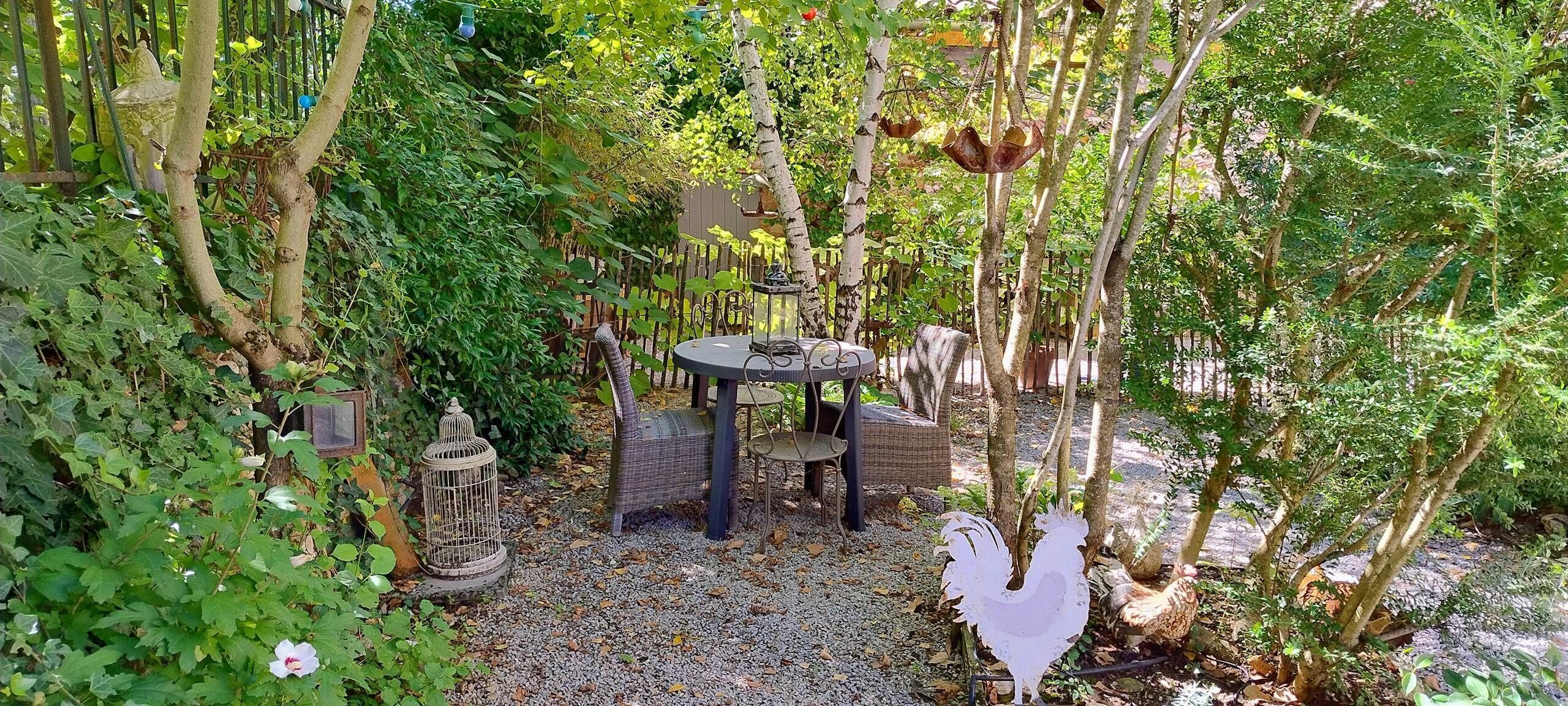 Un espace jardin aménagé avec une table et des chaises, entouré d’arbres et de plantes.