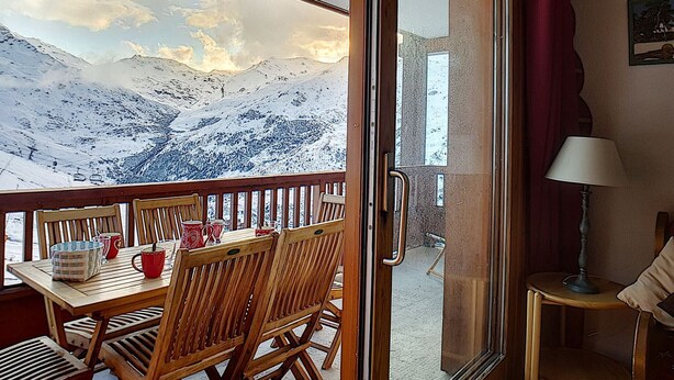 Een houten tafel met stoelen en zicht op een besneeerd berglandschap door een glazen deur.