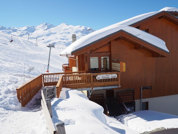 Una cabaña de madera con balcón, con una imponente montaña nevada al fondo.