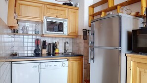 Een kleine keuken met houten kastjes, een ingebouwde magnetron, een roestvrijstalen koelkast en een vaatwasser.