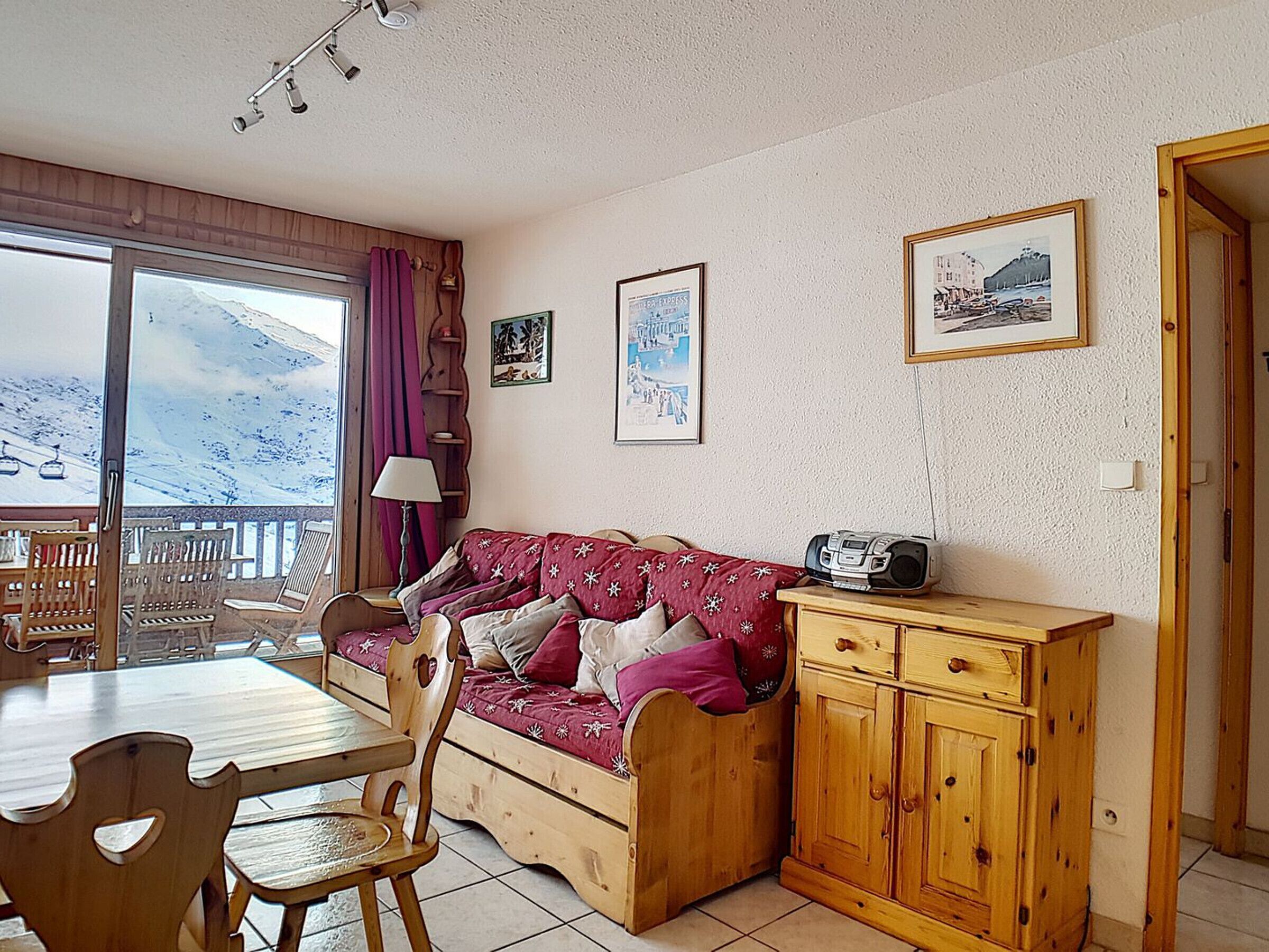 Um quarto acolhedor com um sofá de madeira, uma mesa de jantar com cadeiras, um armário de madeira e uma janela com vista para uma paisagem nevada.