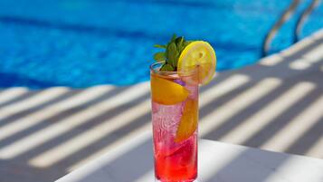 A glass of red drink with lemon and mint on a white table by a pool.