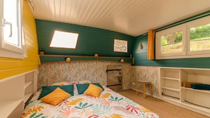 A small, cozy room with a bed, a stool, and a window.