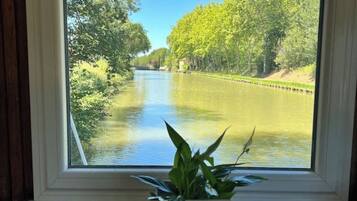 Een raam met uitzicht op een rivier, een bloempot en een toetsenbord op een bureau.