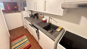 Cocina compacta con gabinetes blancos, encimera negra, un lavamanos y una estufa.
