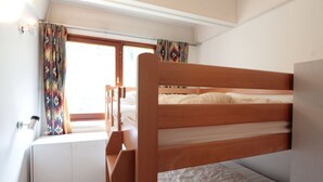 Dormitorio con literas, ventana, cortinas y radiador.