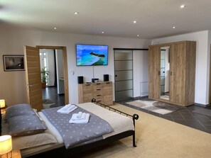 A modern bedroom with a bed, bedside tables, a TV, a wardrobe, and a bathroom visible through an open door. - Luxury 1-bed Apartment in Varazdinske Toplice (Varazdinske Toplice)