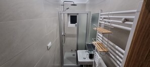 Un baño pequeño con cabina de ducha de vidrio, una ventana y un perchero con repisas.
