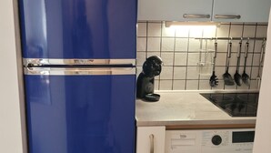 A compact kitchen with a blue refrigerator, a microwave, a washing machine, and a sink with hanging utensils.
