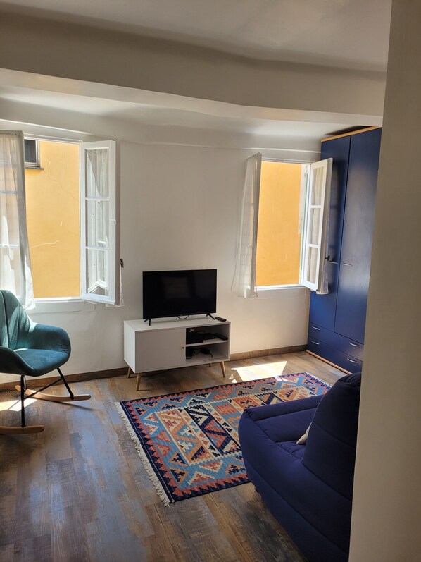 A living room with a television on a white cabinet, a blue sofa, a rocking chair, and a patterned rug.