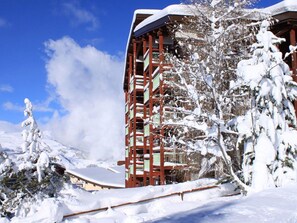 Un edificio cubierto de nieve con fachada roja y blanca, rodeado de árboles cargados de nieve y un cielo azul despejado.