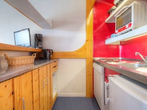 Une cuisine de taille réduite, dotée de meubles en bois, d’un four à micro-ondes, d’une machine à café et d’un évier.