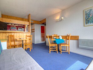 Una habitación con una cama, una mesa de comedor con sillas, una kitchenette y una puerta roja.