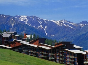 Un hôtel composé de plusieurs bâtiments, chacun doté d’un toit en pente et de grandes fenêtres, le tout se dressant sur un fond de montagnes enneigées.