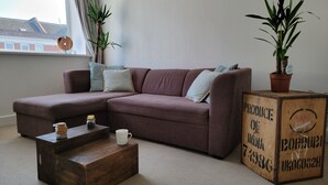A living room with a brown sectional sofa, two potted plants, a wooden coffee table, and a vintage crate with text. - NEW! Rustic Loft Escape Bournemouth (5mins to Beach, Uni, Bars, Shops) Park FREE (Bournemouth)