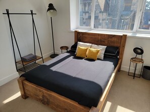 A bedroom with a wooden bed frame, a black and white bedding set, a standing floor lamp, and a view of a building through a window. - NEW! Rustic Loft Escape Bournemouth (5mins to Beach, Uni, Bars, Shops) Park FREE (Bournemouth)