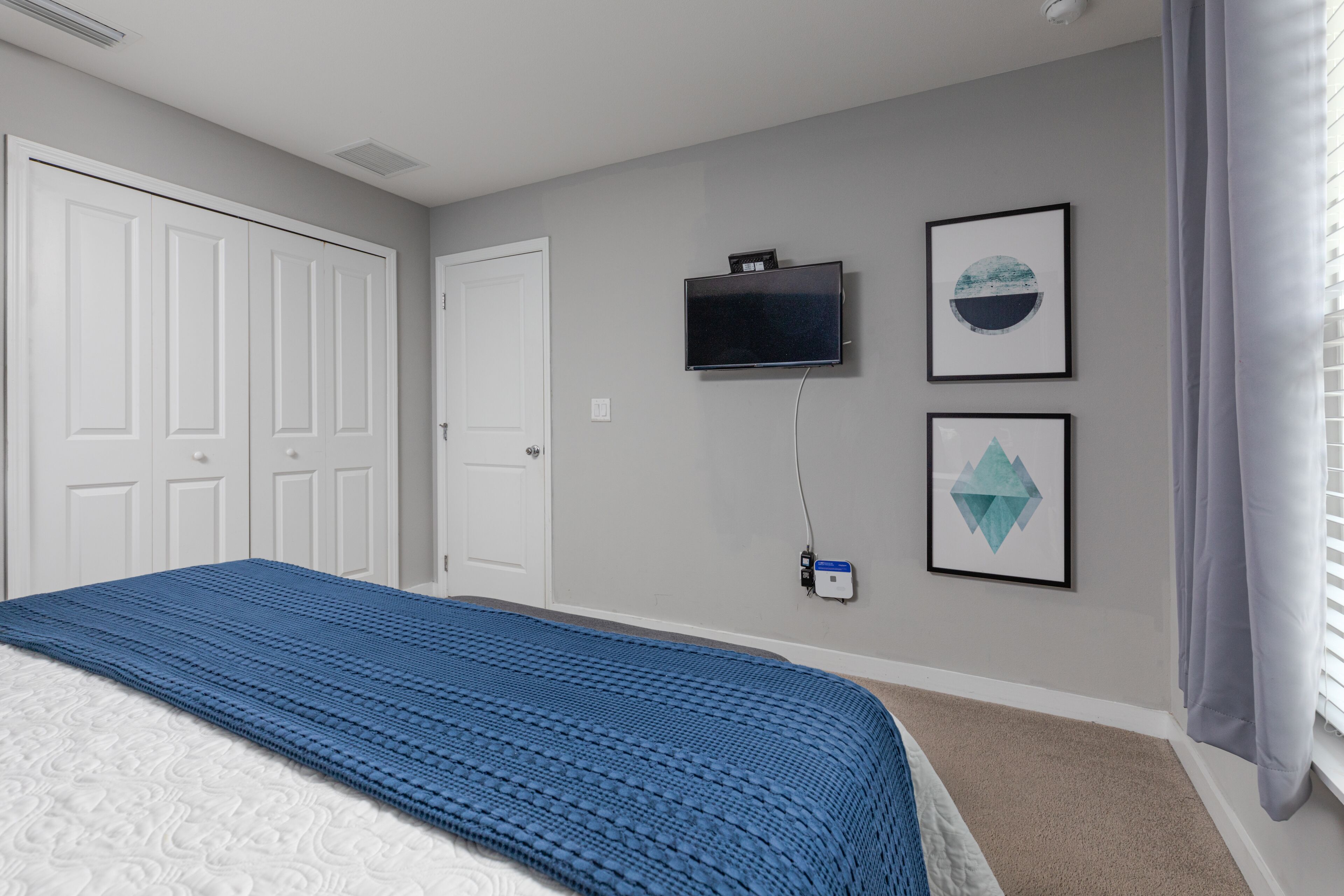 Een slaapkamer met een bed, een aan de muur bevestigde televisie en twee ingelijste kunstwerken.