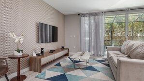Un salon moderne avec un téléviseur, un canapé, une table basse et un tapis à motifs.