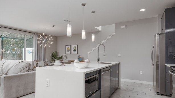 Une cuisine moderne dotée d’un îlot central, d’appareils électroménagers en acier inoxydable et de luminaires suspendus.