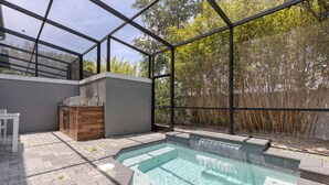 Un espace piscine extérieur moderne, doté d’une structure en verre, d’un barbecue et d’un chemin en pierre.