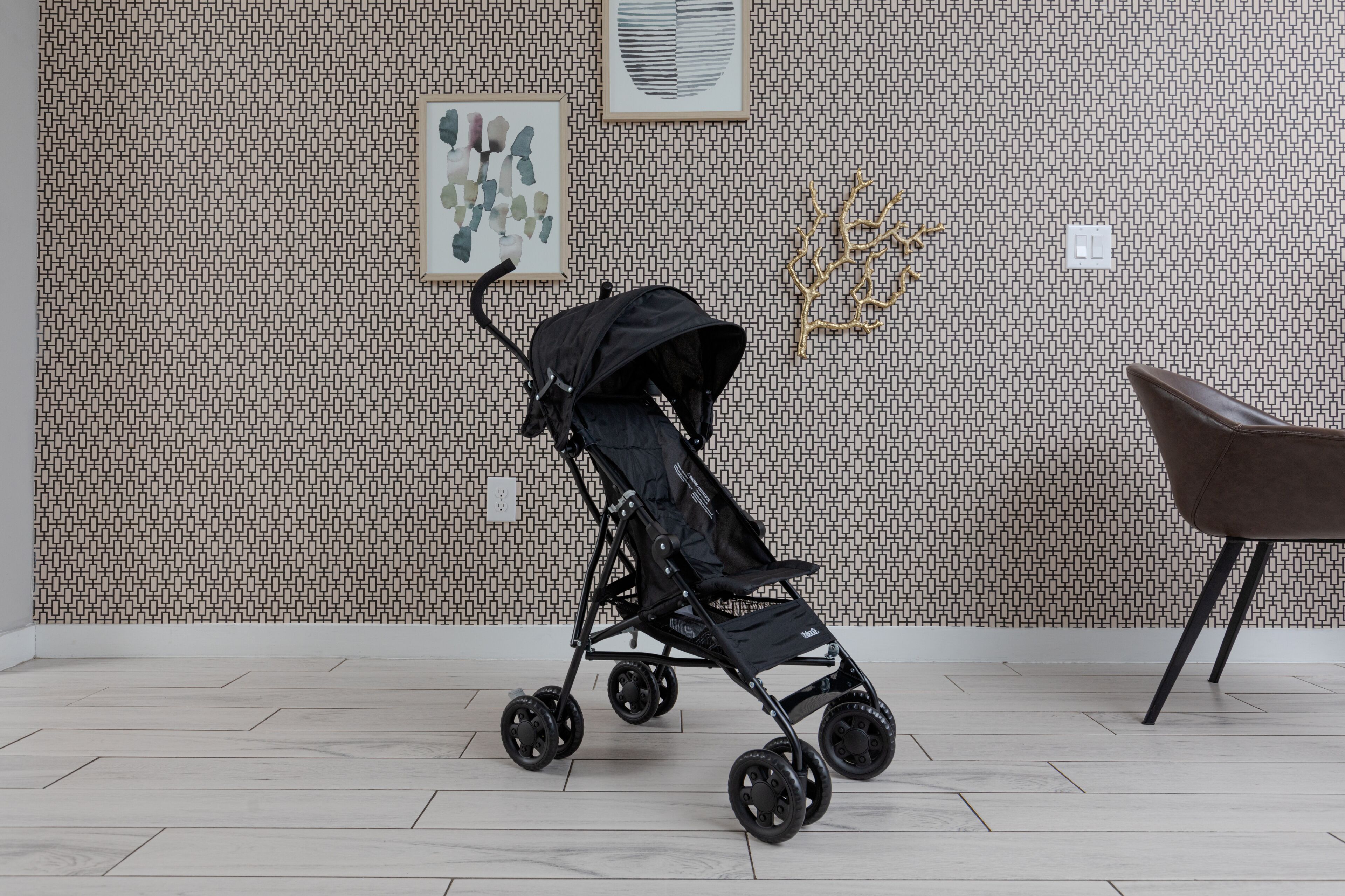 Een kamer met een behang, een zwarte kinderwagen en een bruine stoel.