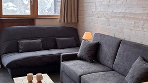 A modern living room with a sectional sofa, a wooden coffee table with two mugs, a lamp, and a view of a snowy landscape through a window. - Cozy 2-room apartment in Avoriaz for 4 people (Avoriaz)