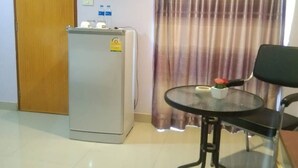 A room with a refrigerator, a table with chairs, a door, and a curtain. - Lucky Inn Residency (Pattaya)