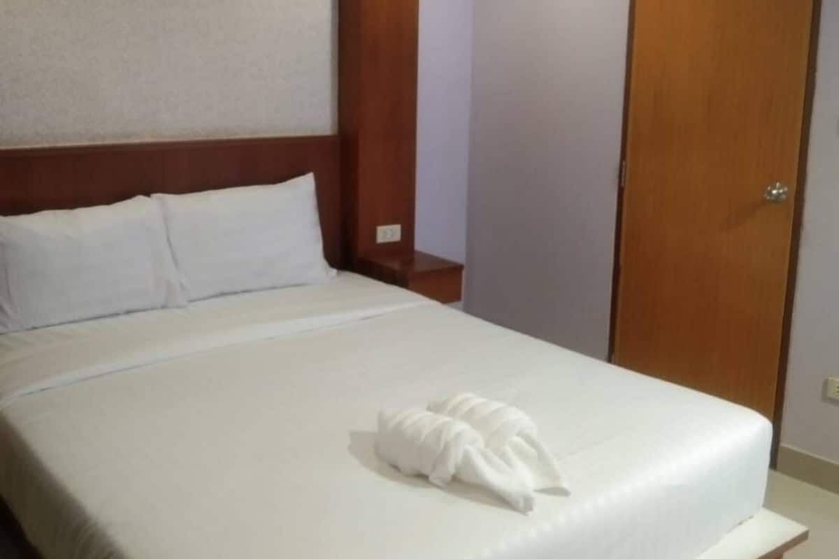 A hotel room with a large bed, wooden headboard, a wooden nightstand, a white pillow, a white towel, a wooden door, and a ceiling fan.