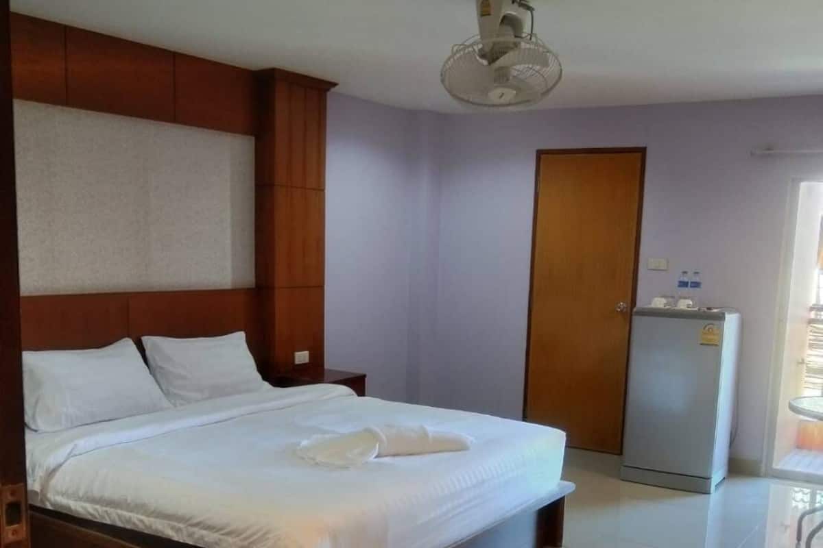 A hotel room with a wooden bed, a ceiling fan, a refrigerator, and a door.