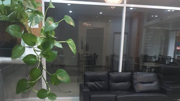 A modern living room with a black leather sofa, a glass partition, and a potted plant. - Lucky Inn Residency (Pattaya)