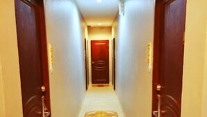A narrow, well-lit hallway with two wooden doors on either side, leading to a room with a red door at the end. - Lucky Inn Residency (Pattaya)