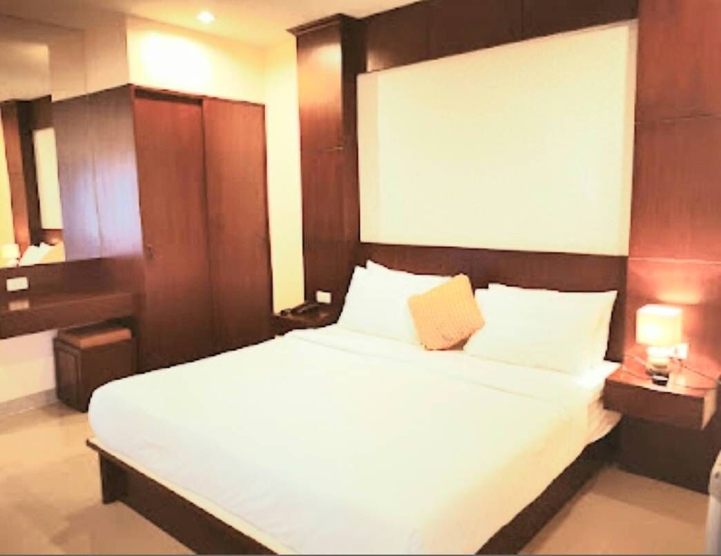 Habitación de hotel con una cama grande, cabecera de madera, mesita de noche con lámpara y armario.