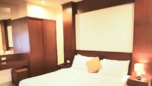 A hotel room with a large bed, wooden headboard, a nightstand with a lamp, and a wardrobe. - Lucky Inn Residency (Pattaya)