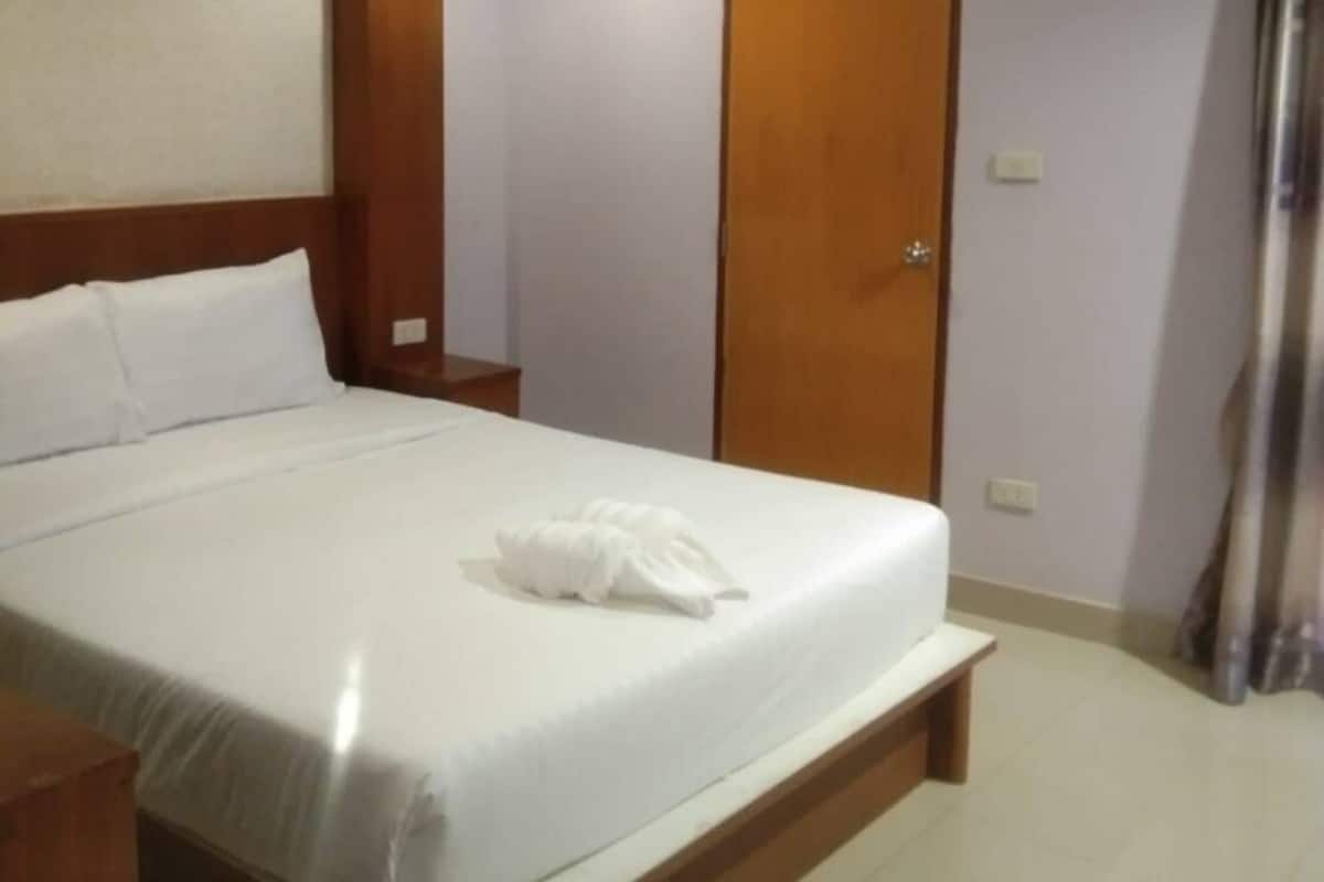 A hotel room with a bed, wooden headboard, a ceiling fan, a door, and a curtain.